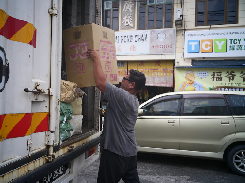 Seorang lelaki memasukkan kotak kadbod ke dalam lori penghantaran berwarna putih