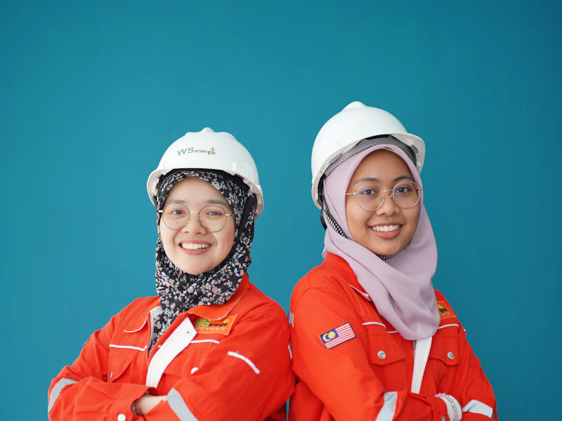 Dua jurutera wanita bertudung memakai topi keselamatan dan baju kerja